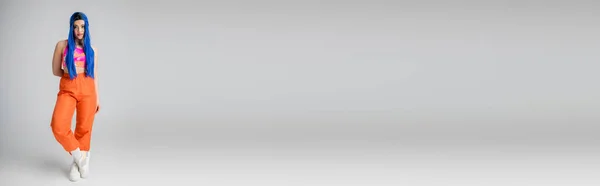 Piena lunghezza della giovane donna con il colore dei capelli blu in posa in abito elegante su sfondo grigio, capelli lunghi, pantaloni arancioni e crop top rosa, moda in avanti, stile personale, individualismo, banner — Foto stock