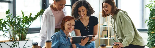 Cheerful multiracial woman showing diary to smiling multicultural female friends holding takeaway drinks in interest club, spending time in friendly and understanding diverse community, banner — Stock Photo