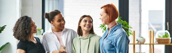 Delighted and stylish multicultural girlfriends smiling at each other while standing in cozy atmosphere of women interest club, mutual support, solidarity and trust concept, banner — Stock Photo