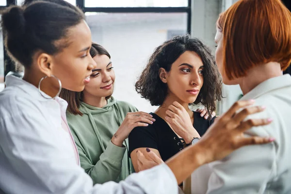 Offended multiracial woman looking away near multicultural female friends and psychologist calming her in consulting room, problem-solving and mutual support concept — Stock Photo
