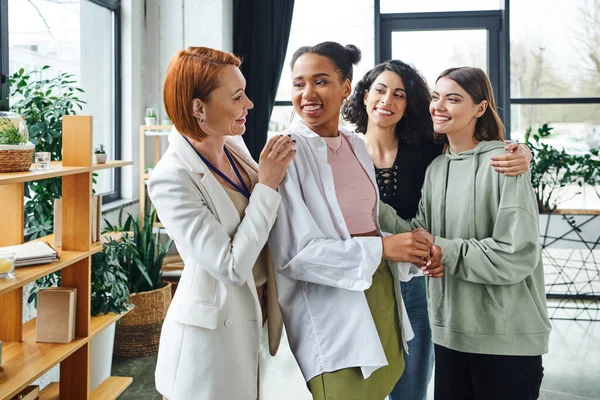 Pleased psychologist looking at overjoyed african american woman near multiethnic girlfriends during motivation session in consulting room, female unity and support concept — Stock Photo