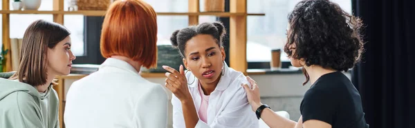 Upset african american woman talking to motivation coach and multicultural female friends during psychology session in consulting room, problem-solving and mental wellness concept, banner — Stock Photo