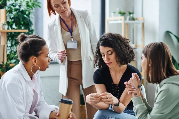 Professional psychologist and young multiethnic girlfriends looking at depressed and frustrated multiracial woman sitting in consulting room, problem-solving and mental wellness concept — Stock Photo