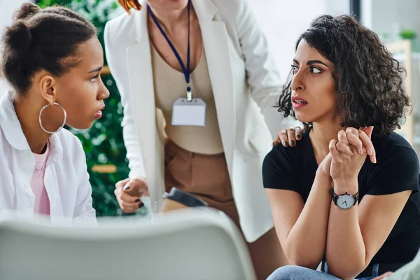 Upset and worried multiethnic woman sitting and looking away near young african american girlfriend during therapy with psychologist, problem-solving and mental wellness concept — Stock Photo