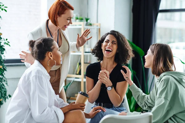 Psychologue heureux geste près excité femme multiraciale rire les yeux fermés lors de la séance de motivation avec des copines multiethniques, la compréhension, le soutien et la santé mentale concept — Photo de stock
