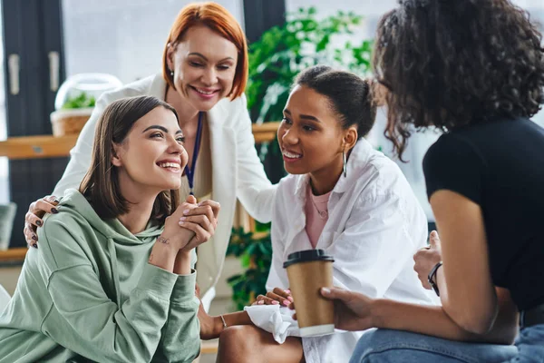 Inspired and excited woman sitting and talking to multiethnic female friends and smiling psychologist during supportive session in consulting room, motivation and mental wellness concept — Stock Photo