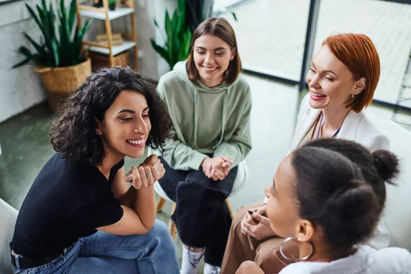 High angle view of cheerful multiracial woman talking to african american girlfriend near smiling psychologist during group therapy in consulting room, communication and mental wellness concept — Stock Photo