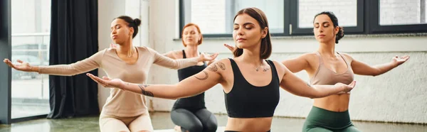 Diverse multicultural female friends in sportswear practicing yoga and meditating with closed eyes and outstretched hands, inner peace and body awareness concept, banner — Stock Photo