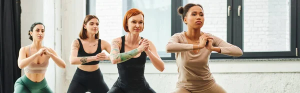 Achtsamkeit und Inspiration, vielfältige Gruppe multikultureller Frauen, die nach vorne schauen, während sie mit geballten Händen während des Yoga-Kurses meditieren, Harmonie und Konzept für psychische Gesundheit, Banner — Stockfoto