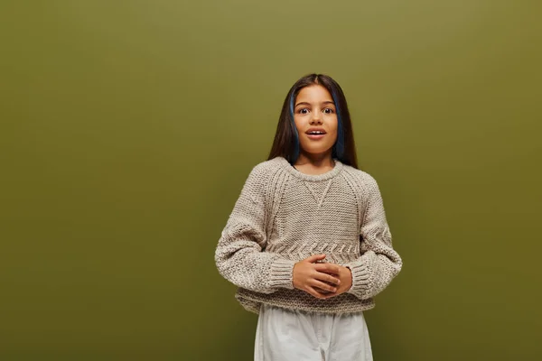 Excited brunette preteen girl with dyed hair in stylish knitted sweater and casual clothes looking at camera while standing isolated on green, contemporary fashion for preteen concept — Stock Photo