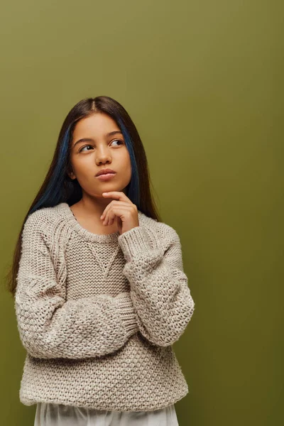 Pensive brunette preteen girl with dyed hair wearing stylish knitted sweater and looking away while standing isolated on green, fashion-forward preteen with sense of style — Stock Photo