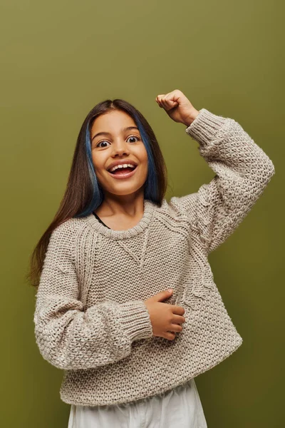 Excited and stylish preteen girl with dyed hair wearing knitted sweater while looking at camera and showing yes gesture isolated on green, fashion-forward preteen with sense of style — Stock Photo