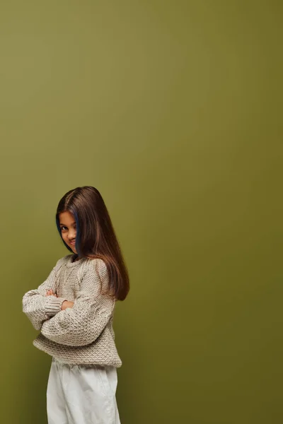Оскорбленная и стильная девочка-подросток с цветными волосами в трикотажном свитере и скрещивая руки стоя и позируя изолированно на зеленом, модном форварде с чувством стиля — стоковое фото