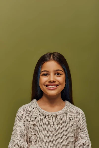 Портрет положительной и стильной брюнетки юной девушки с окрашенными волосами в современном уютном трикотажном свитере, глядя в камеру, находясь в изоляции на зеленой, современной моде — стоковое фото