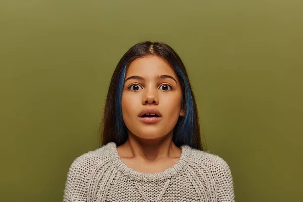 Portrait de preteen girl effrayée et élégante avec des cheveux teints portant un pull tricoté et regardant la caméra tout en se tenant debout et posant isolé sur vert, mode préadolescente moderne — Photo de stock