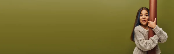 Criança pré-adolescente excitada e na moda com cabelo tingido vestindo camisola de malha e olhando para a câmera enquanto abraça papel laminado isolado em verde, menina irradiando vibrações de outono, banner — Fotografia de Stock