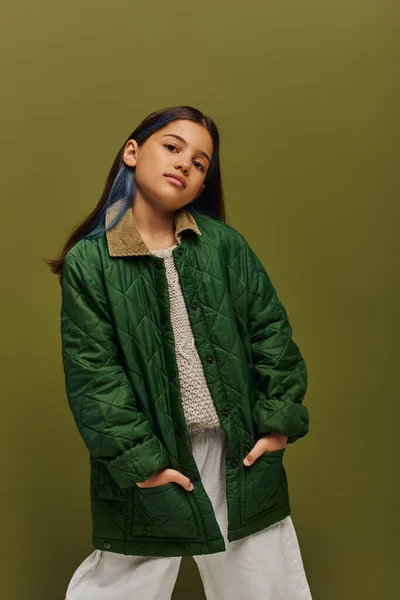 Уверенная и стильная брюнетка-подросток с окрашенными волосами, позирующая в осеннем наряде и вязаном свитере и смотрящая на камеру, изолированную на зеленой, современной осенней моде для подростков — стоковое фото