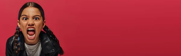 Porträt eines verrückten und stilvollen vorpubertären Mädchens mit Frisur, die in die Kamera schreit und in Lederjacke auf Rot posiert, Frisur und trendiges Accessoire-Konzept, Banner — Stockfoto