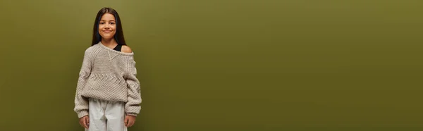 Ragazza bruna preadolescente alla moda in maglione lavorato a maglia e vestito autunnale guardando la fotocamera mentre in piedi e in posa isolata sul concetto di vibrazioni autunnali verdi e rilassate, banner — Foto stock