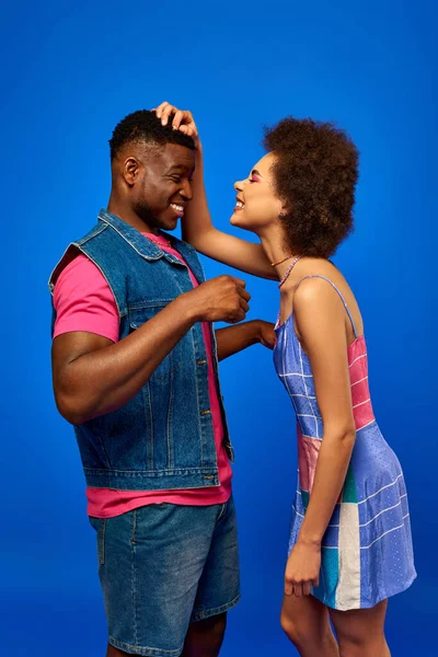 Cheerful young african american woman in sundress having fun with stylish best friend while spending time and standing together isolated on blue, best friends in matching outfits, friendship — Stock Photo