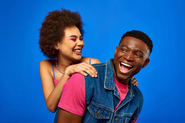 Sorrindo jovem afro-americana com maquiagem ousada abraçando melhor amigo na moda em roupa de verão e passar o tempo juntos isolado em azul, melhores amigos em roupas correspondentes, amizade — Fotografia de Stock