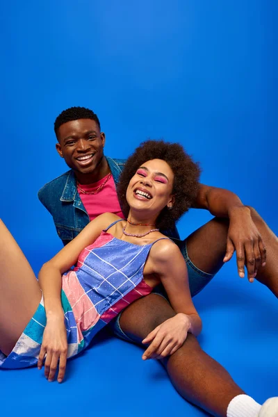 Alegre e na moda jovens afro-americanos melhores amigos em roupas de verão brilhante olhando para a câmera enquanto posando juntos em fundo azul, besties na moda irradiando confiança — Fotografia de Stock