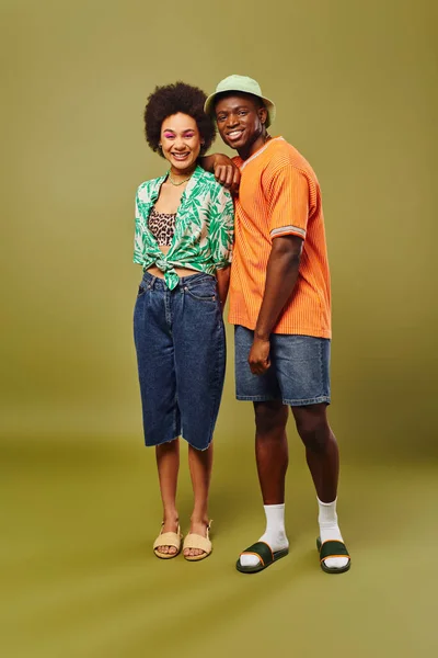 Full length of trendy young african american best friends in summer shorts and outfits looking at camera while standing on olive background, friends showcasing individual style, friendship — Stock Photo
