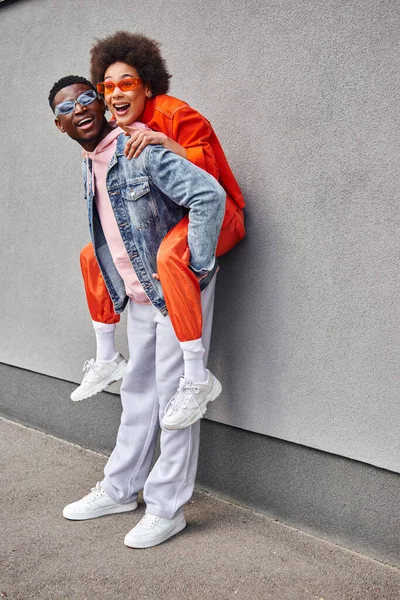 Возбужденная африканская американка в солнечных очках и стильном наряде, указывающая пальцем на лучшего друга, стоя рядом со зданием на городской улице, дружит с модной эстетикой — стоковое фото