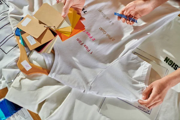 Вид зверху на молодих багатоетнічних дизайнерів, що тримають друкарський шар і кольорові годинники, при роботі з одягом на столі в друкованій студії, концепція можливості самозайнятості — стокове фото