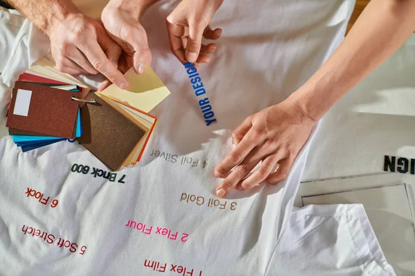 Обзор молодых мультиэтнических дизайнеров, работающих с цветными образцами и печатными слоями рядом с одеждой на столе во время проекта в типографии, концепция возможности самостоятельного трудоустройства — стоковое фото