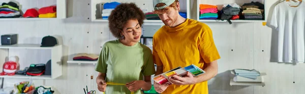 Jeunes designers multiethniques travaillant ensemble avec des échantillons de couleurs et de ruban à mesurer pendant le projet dans un studio d'impression floue en arrière-plan, concept d'opportunité de travail indépendant, bannière — Photo de stock