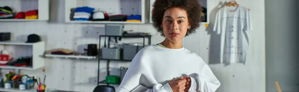 Portrait of young and confident african american craftswoman looking at camera while standing in blurred print studio at background, enthusiastic business owner working in workshop, banner — Stock Photo