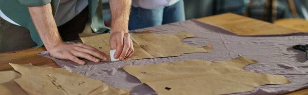 Cropped view of craftsman marking cloth near sewing patterns and blurred colleague while working in print studio, collaborative business owners working together, banner — Stock Photo