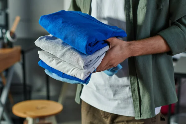 Cropped view of young craftsman holding clothes while standing and working in print studio at background, customer-focused entrepreneur concept — Stock Photo