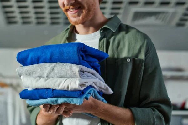 Cropped view of smiling blurred young craftsman holding clothes while standing and working in print studio at background, customer-focused entrepreneur concept — Stock Photo