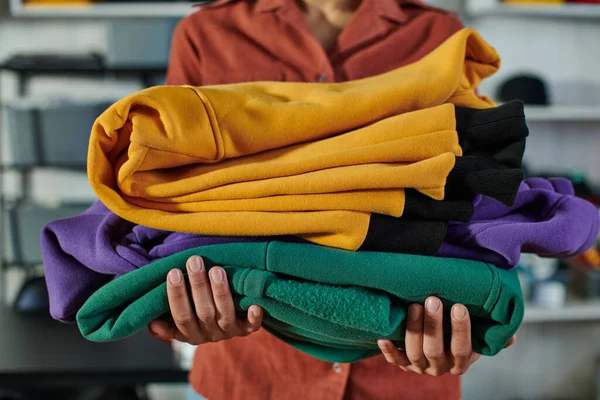 Ausgeschnittene Ansicht eines verschwommenen jungen afrikanisch-amerikanischen Kunsthandwerkers, der Kleidung hält, während er im Druckstudio steht und arbeitet, kundenorientiertes Unternehmerkonzept — Stockfoto