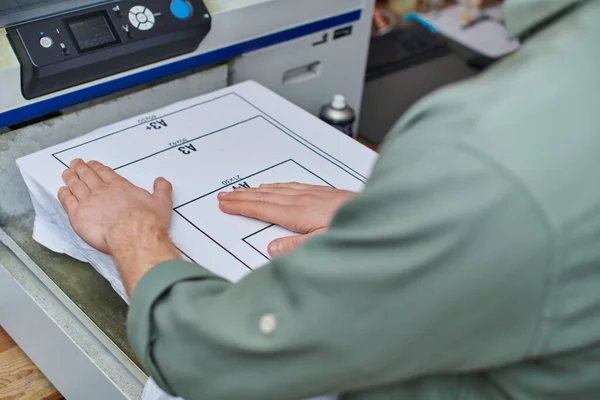 Ausgeschnittene Ansicht junger Handwerker bei der Arbeit mit T-Shirt mit Markierung und Siebdruckmaschine im Druckereistudio, kundenorientiertes Kleinunternehmenskonzept, Grafikdesign — Stockfoto