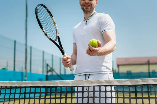 Vue recadrée de l'homme en vêtements de sport tenant raquette de tennis et ballon près du filet, joueur, passe-temps et sport — Photo de stock
