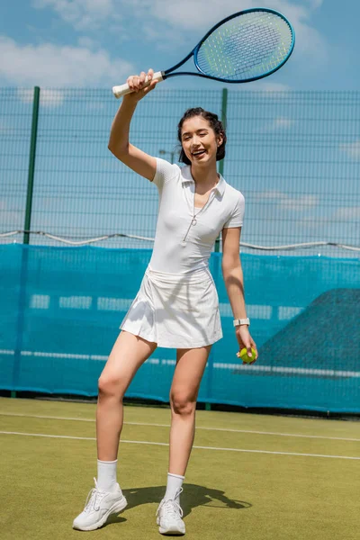 Полная длина, веселая женщина в спортивной одежде держа ракетку и мяч, мотивация и спорт — стоковое фото