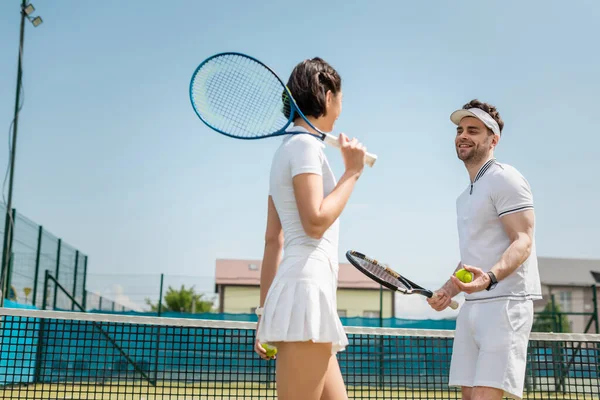 Positive couple holding tennis balls and rackets on court, hobby and summer leisure, sport — Stock Photo