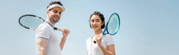 Banner, happy couple in sportswear standing with tennis rackets on court, looking at camera, sport — Stock Photo