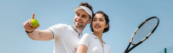 Banner, happy man pointing away near girlfriend on tennis court, holding racket, sport and romance — Stock Photo