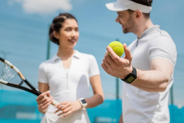 Focus on ball, blurred man looking at girlfriend, teaching how to play tennis on court, sport — Stock Photo