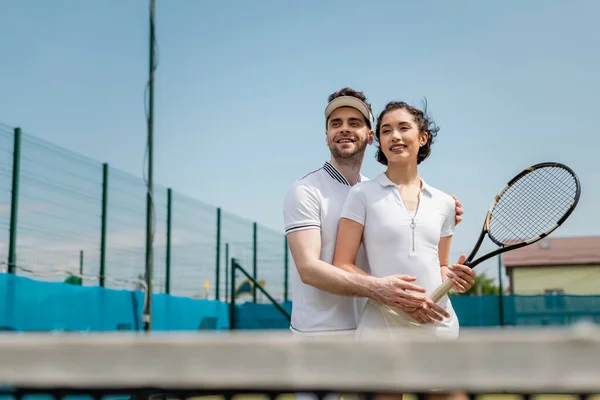 Romance on tennis court, happy man teaching girlfriend how to play tennis, summer sport — Stock Photo