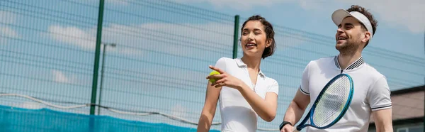 Bannière, femme heureuse pointant du doigt, homme souriant et tenant une raquette de tennis, été, sport de couple — Photo de stock