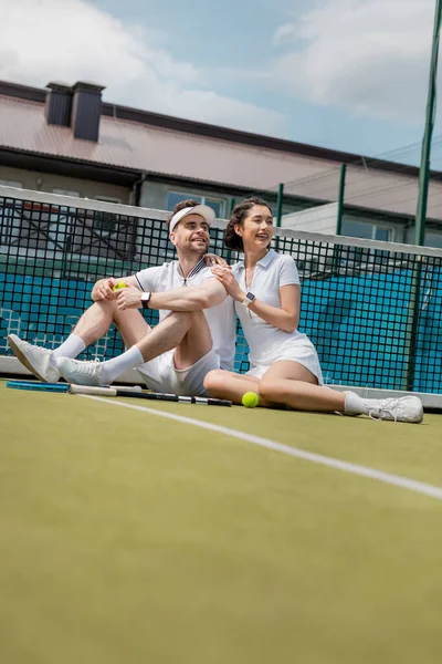 Веселий чоловік і жінка, що сидить біля тенісної мережі, ракетки і м'яч, літній спорт, дозвілля і розваги — стокове фото