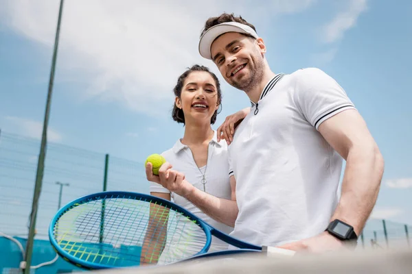 Позитивная пара, смотрящая на камеру, теннисную ракетку и мяч, летние развлечения, отдых и развлечения — стоковое фото