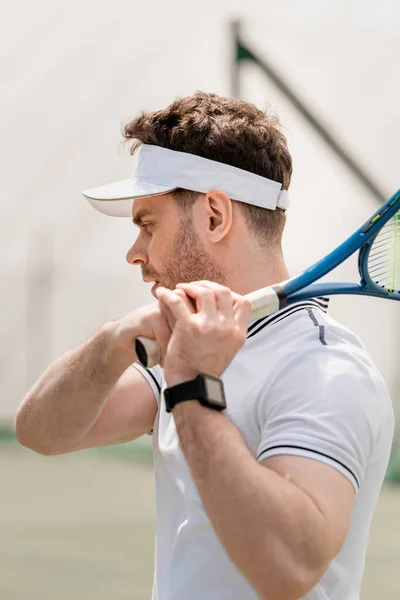 Guapo tenista en visera deportiva sosteniendo raqueta en pista, motivación y deporte - foto de stock