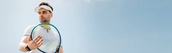 Баннер, красивый мужчина в активной одежде и козырьковой шапке проведение теннисной ракетки на корте, спорт и досуг — стоковое фото