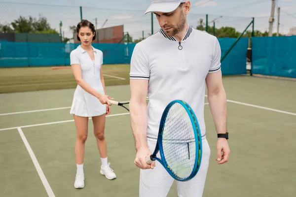 Мужчина в активной одежде проведение теннисной ракетки и тренировки с подругой на корте, мотивация, спорт — стоковое фото